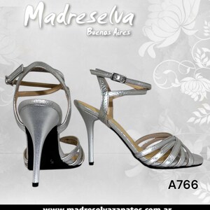 May include: A pair of silver metallic high-heeled sandals featuring thin crisscross straps across the toe, a slim stiletto heel, and an adjustable ankle strap with a metal buckle. The text Madreselva Buenos Aires and A766 are visible.