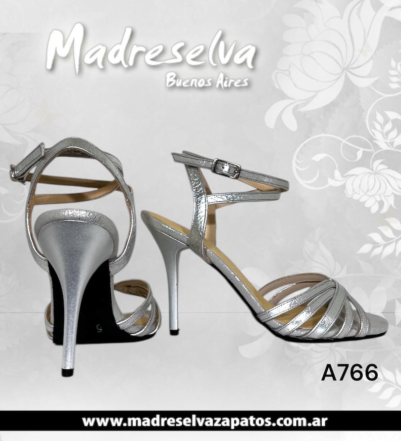 May include: A pair of silver metallic high-heeled sandals featuring thin crisscross straps across the toe, a slim stiletto heel, and an adjustable ankle strap with a metal buckle. The text Madreselva Buenos Aires and A766 are visible.