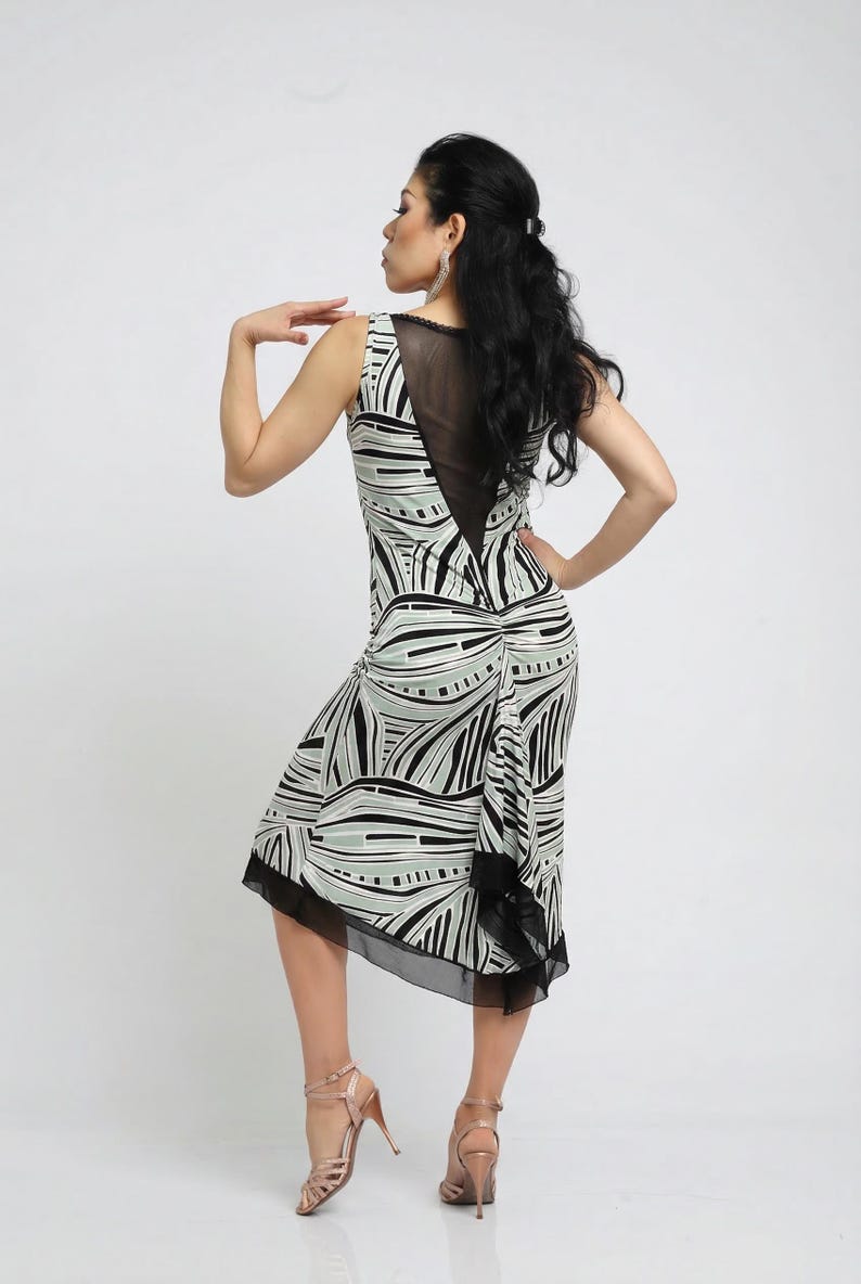 May include: Sleeveless dress with a black, white, and light green abstract pattern. The dress features a sheer black panel on the upper back and a black trim at the hem. The model is wearing high-heeled sandals.