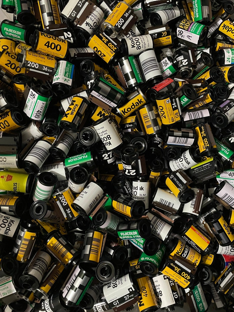 Pu&ograve; includere: Un'immagine ravvicinata di una variet&agrave; di cassette di pellicola in vari colori e dimensioni. Le cassette sono per lo pi&ugrave; gialle e nere con testo e numeri bianchi. Alcune delle cassette hanno il nome del marchio "Kodak" stampato su di esse.