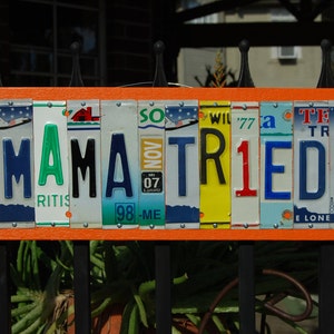 May include: Orange sign with the words "MAMA TRIED" spelled out using license plates. The plates are various colors and have different state abbreviations.