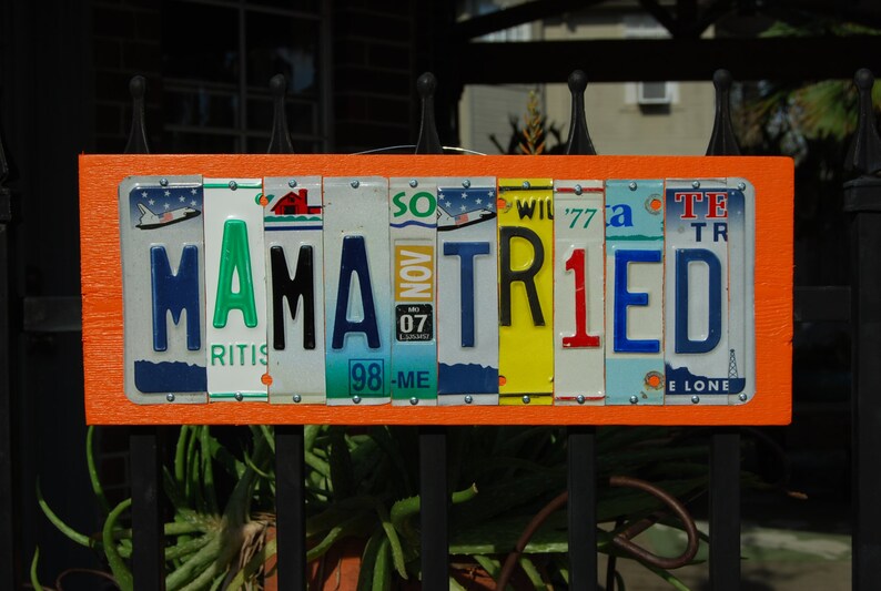 May include: Orange sign with the words "MAMA TRIED" spelled out using license plates. The plates are various colors and have different state abbreviations.