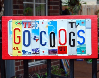 May include: A red wooden sign with the words "GO COOGS" spelled out using license plates. The plates are from different states and have various designs.