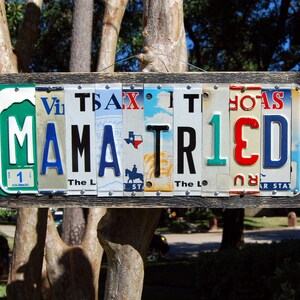 May include: A wooden sign with the words "MAMA TRIED" spelled out using vintage license plates. The plates are in various colors and have different state names and numbers on them.