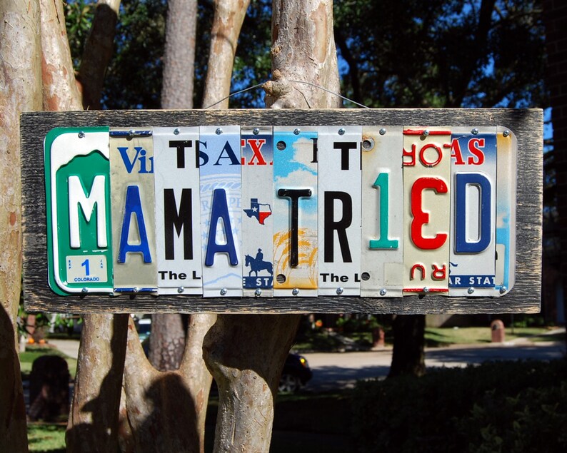 May include: A wooden sign with the words "MAMA TRIED" spelled out using vintage license plates. The plates are in various colors and have different state names and numbers on them.