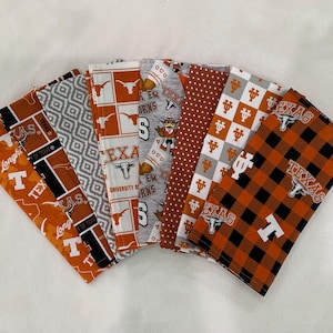 May include: A collection of seven fabric items, each featuring a different pattern and design. The color palette includes orange, white, gray, and black. The items display the text "TEXAS" and the Longhorn logo, indicating a theme related to the University of Texas.