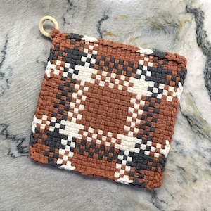 May include: A brown, white and grey woven pot holder with a wooden loop handle.