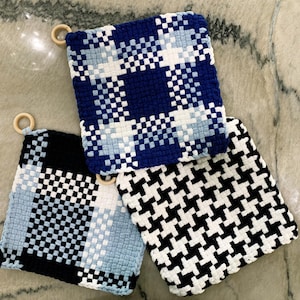 Puede incluir: Tres salvamanteles cuadrados tejidos con diferentes patrones. Uno es a cuadros azules y blancos, otro con estampado de pata de gallo en blanco y negro, y el tercero es una mezcla de negro, blanco y azul. Cada uno tiene un anillo de madera.