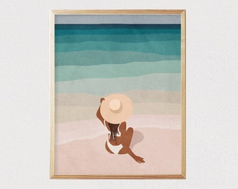 May include: A woman in a white swimsuit and a wide-brimmed straw hat sits on a pink sandy beach facing the ocean. The ocean is a gradient of blue and green.