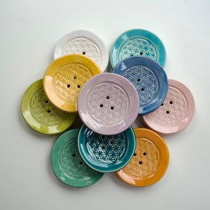 Könnte beinhalten: Ein Set aus neun Keramik-Seifenschalen in verschiedenen Farben, jede mit einem erhabenen geometrischen Muster. Die Schalen sind in einem Kreis angeordnet, wobei die Farben von Gelb über Grün und Blau bis Rosa reichen.