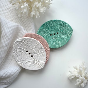 May include: Three ceramic soap dishes in leaf shapes with a paisley pattern. The dishes are white, pink, and teal.