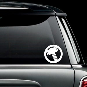 May include: A white vinyl decal of Thor's hammer in a circle on a black car.