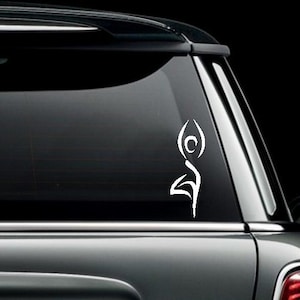 May include: A white vinyl decal of a stylized yoga pose on a silver car. The decal is on the back window of the car.