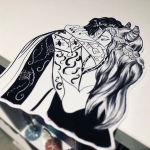K&ouml;nnte beinhalten: Schwarz-wei&szlig;-Illustration von zwei Figuren, die sich umarmen. Die Figur links tr&auml;gt einen langen Mantel mit aufwendigen Blumendesigns. Die Figur rechts hat langes Haar und H&ouml;rner.