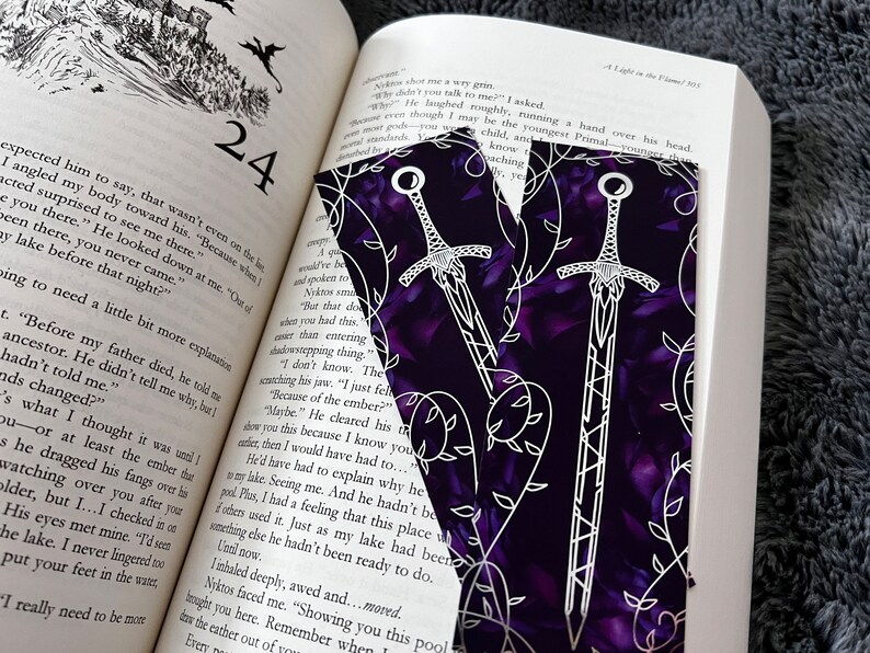 K&ouml;nnte beinhalten: Zwei violette Lesezeichen mit einem wei&szlig;en Schwertmuster und einem Rankenmuster. Die Schwerter sind wei&szlig; umrandet und haben ein detailliertes Design. Der Hintergrund ist dunkelviolett mit einem dezenten Blumenmuster.