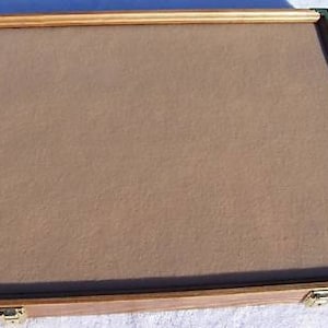 May include: A wooden display case with a brown felt lining and brass corner accents. The case has a hinged lid and two brass clasps.