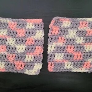 Peut inclure: Deux carrés crochetés en rose, blanc et gris. Les carrés sont réalisés avec un motif de point simple et ont un aspect doux et texturé.