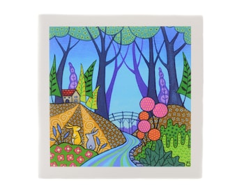 May include: A square ceramic tile featuring a colorful, whimsical forest scene. The artwork depicts a house, bridge, and a winding river, with two rabbits in the foreground. The color palette includes blues, greens, and pinks.