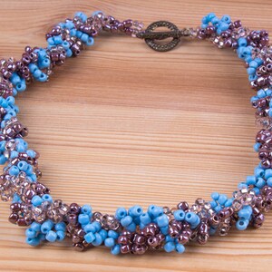 Könnte beinhalten: Eine Perlenkette mit einem Spiraldesign. Die Kette ist aus blauen, braunen und klaren Perlen gefertigt.