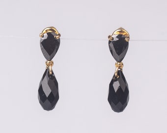 May include: A pair of gold earrings with black teardrop-shaped crystals. The earrings have a small heart-shaped crystal at the top of each teardrop.