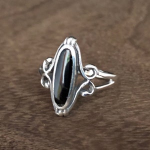 Op de afbeelding: Een zilveren ring met een ovale zwarte edelsteen in een delicaat filigraan ontwerp.