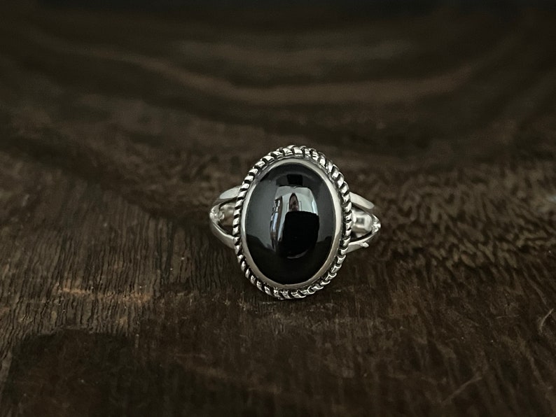 May include: A silver ring with a black oval gemstone set in a rope-like border.
