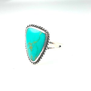 May include: A turquoise ring with a silver setting. The turquoise is a triangular shape and has a marbled pattern. The ring is set in a silver band with a decorative edge.