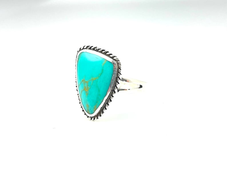 May include: A turquoise ring with a silver setting. The turquoise is a triangular shape and has a marbled pattern. The ring is set in a silver band with a decorative edge.