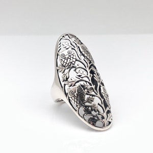 Könnte beinhalten: Ein silberner Ring mit einem filigranen Design aus Eulen und Ästen. Der Ring ist oval geformt und hat ein durchbrochenes Design.
