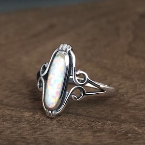 May include: A silver ring with an oval-shaped opal gemstone set in a delicate filigree design.