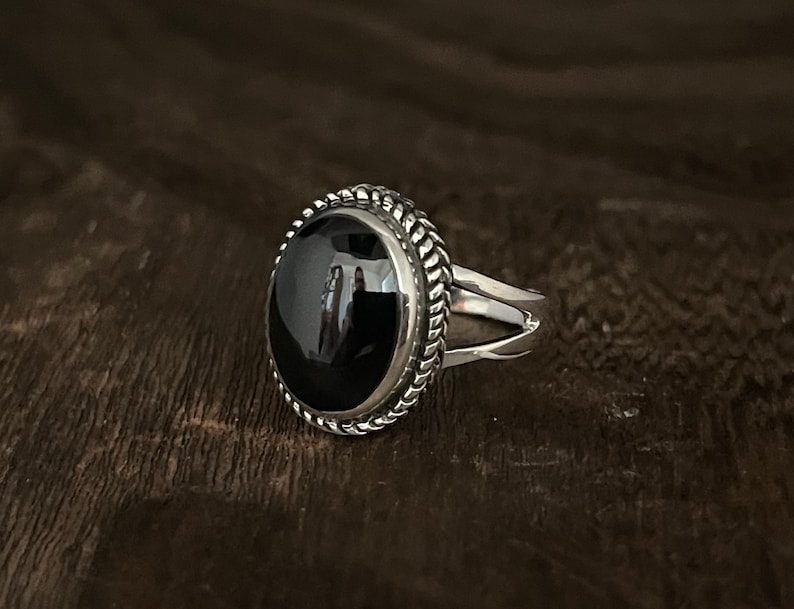 May include: A silver ring with a black oval gemstone set in a rope-like border.