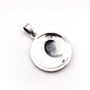 May include: Silver pendant with a round shape and a crescent moon design. The back of the pendant has the number 925 stamped on it.