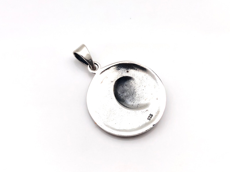 May include: Silver pendant with a round shape and a crescent moon design. The back of the pendant has the number 925 stamped on it.