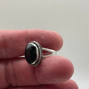May include: A silver ring with a black oval gemstone set in a braided silver bezel.