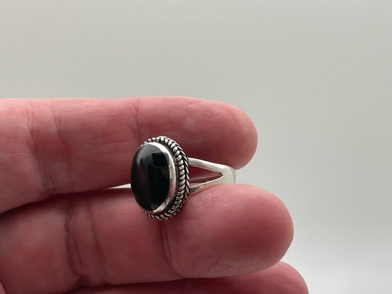 May include: A silver ring with a black oval gemstone set in a braided silver bezel.