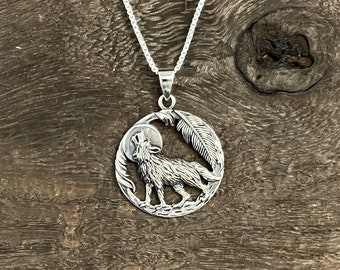 Könnte beinhalten: Silberner Anhänger mit Halskette, der einen Wolf zeigt, der zum Mond heult, mit einem Federdesign. Der Anhänger ist rund und hat ein detailliertes Design.
