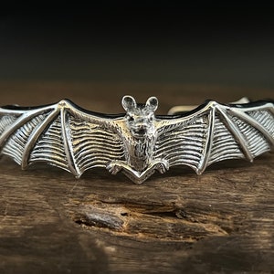 May include: A silver bat-shaped bracelet with detailed wings and a textured surface.