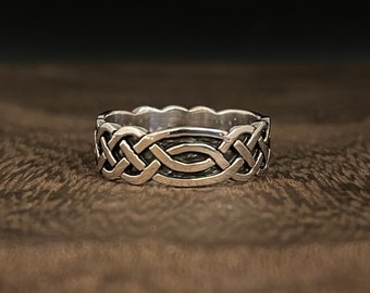 May include: A silver ring with a Celtic knot design. The ring is wide and has a smooth, polished finish.
