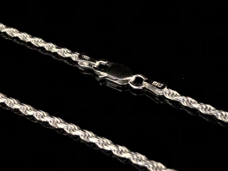 May include: A silver rope chain necklace with a lobster clasp closure. The chain is made of a twisted rope design.