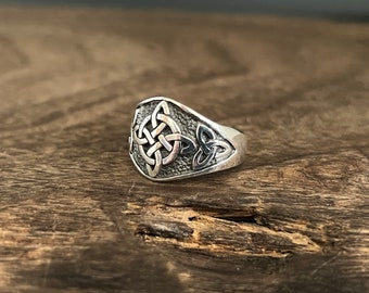May include: A silver ring with a Celtic knot design. The knot is in the center of the ring and is surrounded by a textured band.