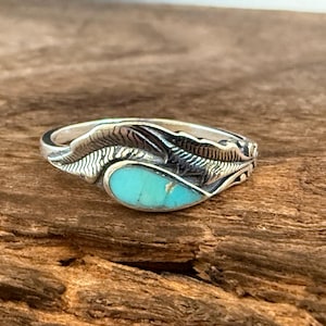 May include: A silver ring featuring a polished, teardrop-shaped turquoise stone inlay set within a textured, leaf-inspired metal band. The silver metal displays intricate, etched detailing that mimics the veins and structure of a natural leaf.