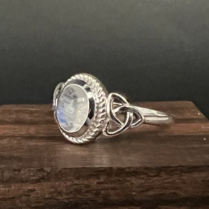 May include: A silver ring featuring a moonstone set within a Celtic knot design.