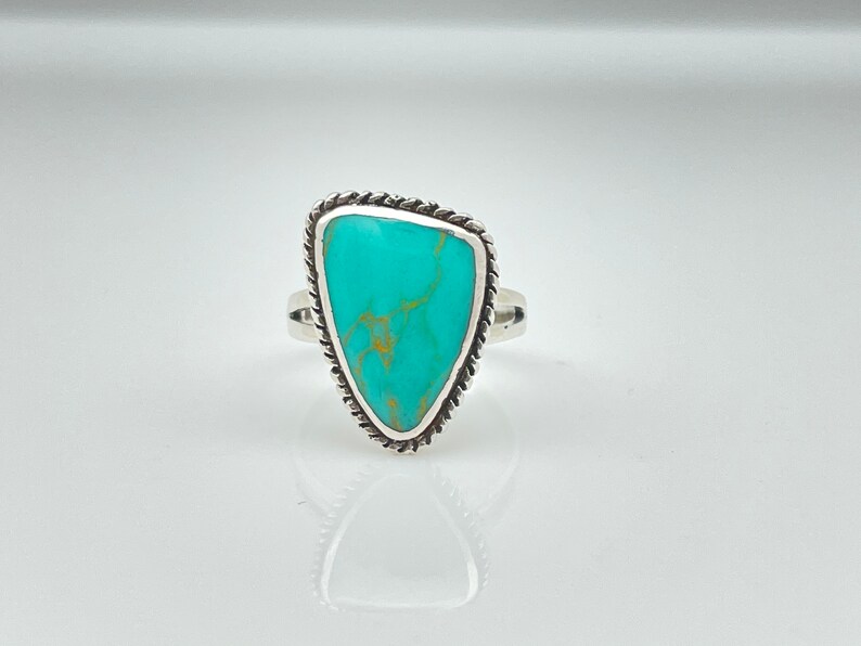 May include: A turquoise ring with a silver setting. The turquoise is a light blue color with brown veins running through it. The ring is a size 7.