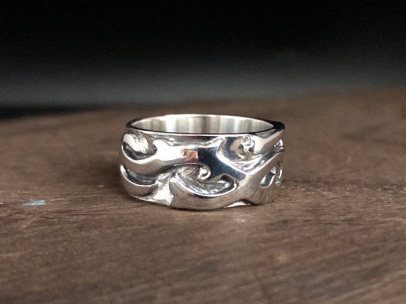 May include: A silver ring with a wave-like design. The ring is wide and has a textured surface.
