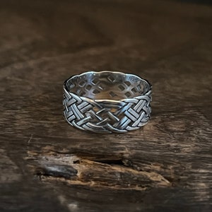 Puede incluir: Un anillo de plata con un diseño tejido. El anillo está marcado con "925" en el interior.
