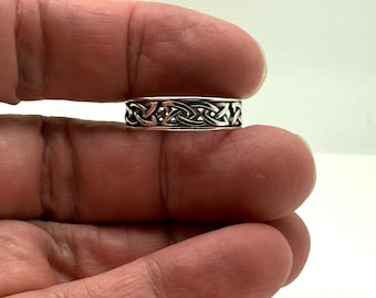 May include: A silver ring with a Celtic knot design. The ring features an intricate pattern of interwoven lines, creating a continuous, symmetrical design. The ring is approximately 0.25 inches wide.