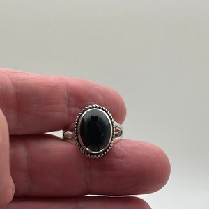 May include: A silver ring with a black oval gemstone set in a twisted silver band.