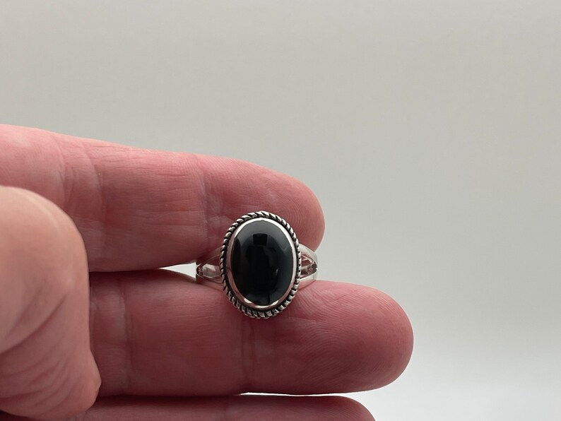 May include: A silver ring with a black oval gemstone set in a twisted silver band.