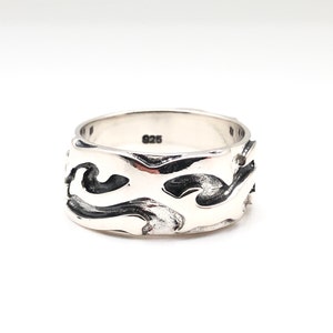 May include: A silver ring with a wide band featuring a wavy, abstract design. The ring is marked with "925" on the inside.