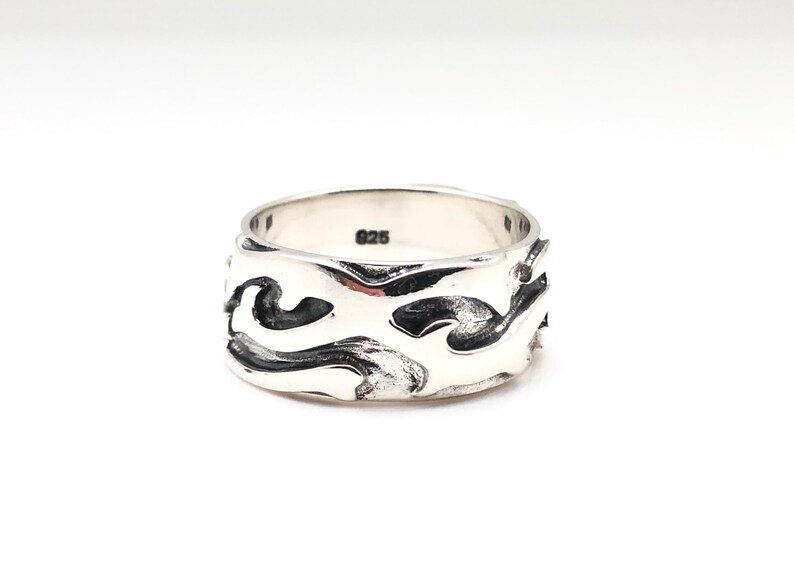 May include: A silver ring with a wide band featuring a wavy, abstract design. The ring is marked with "925" on the inside.